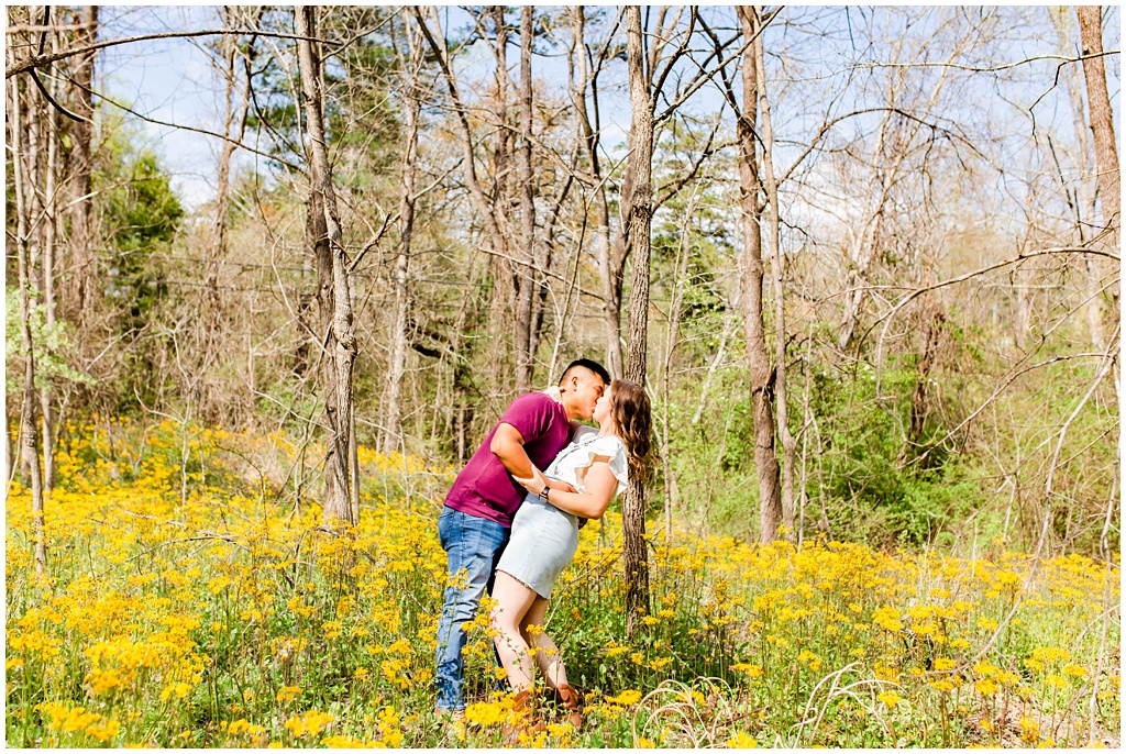 Couple kissing while dipping her backwards in a field of yellow wildflowers.