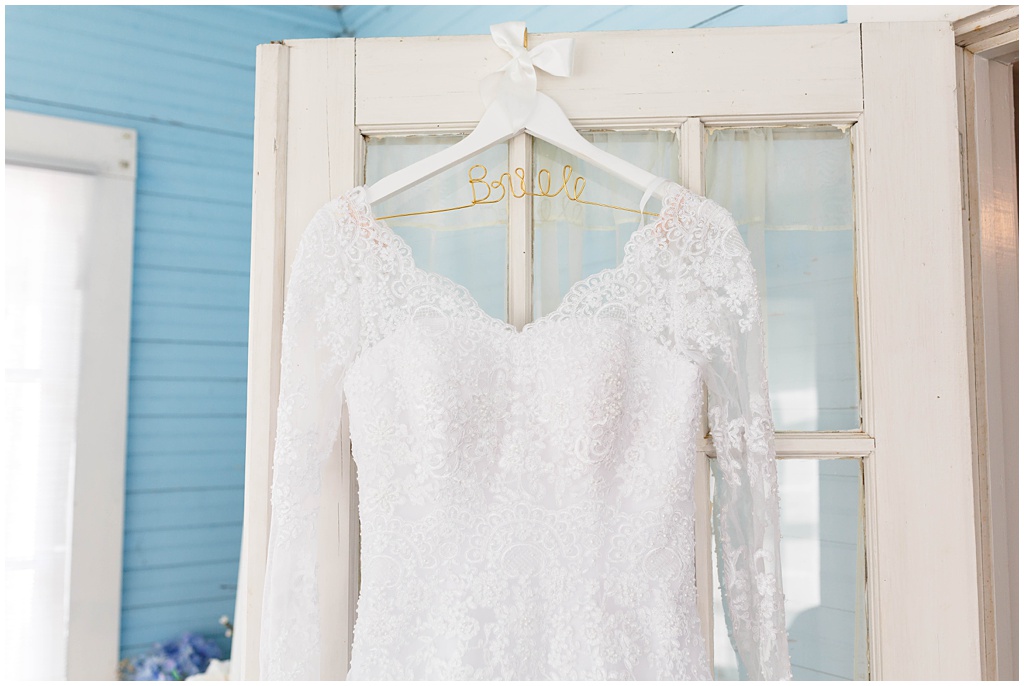 The bride's vintage lace wedding gown hanging on the door of the light blue parlor room at New Beginnings Historic Farm.