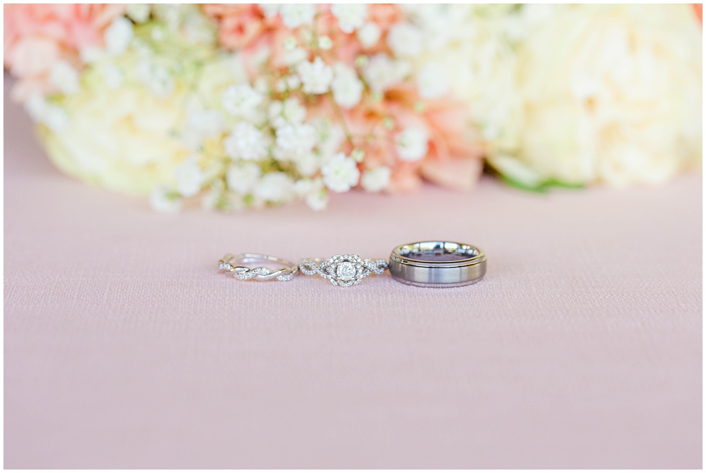 The bride's rings and groom's wedding band with hints of pink and coral florals.