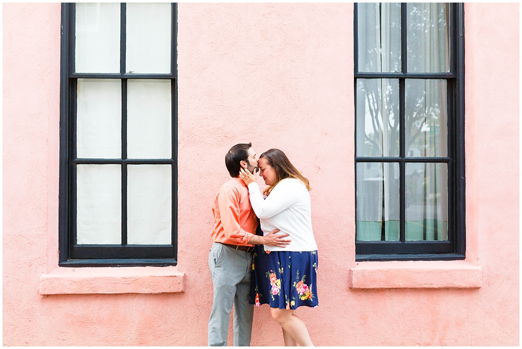 The couple shares a kiss in front of a pink wall.