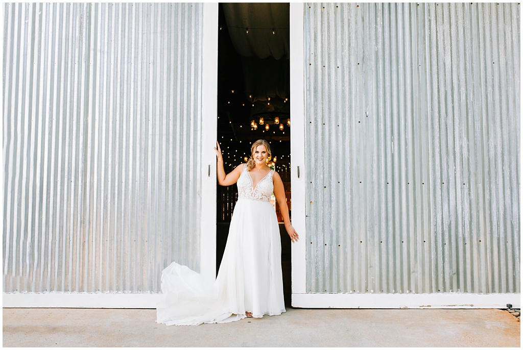 Bridal portrait in front of the reception barn with aluminum barn doors and twinkle lights.