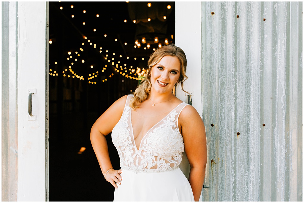 Bridal portrait in front of the reception barn with aluminum barn doors and twinkle lights.