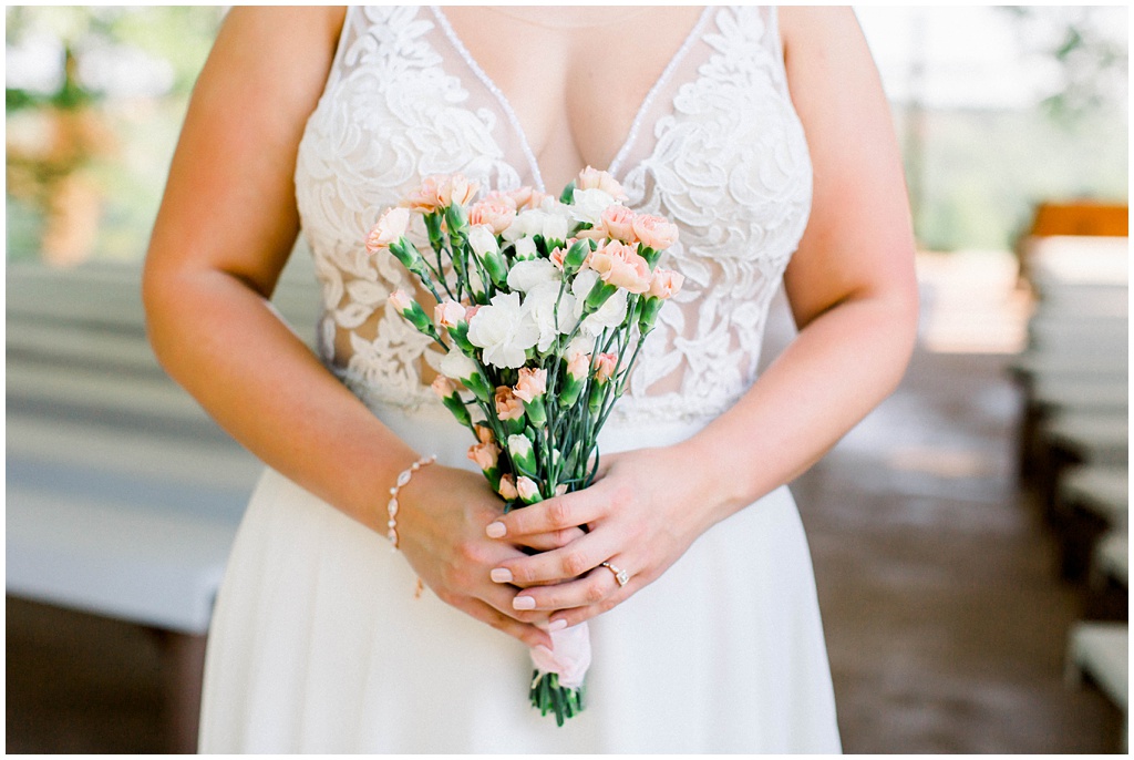 The bride holds a bouquet of white and peach carnations.