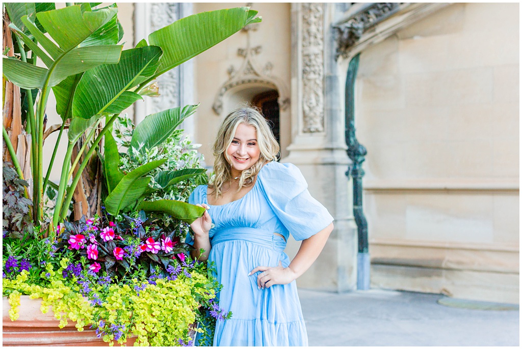 blonde headed girl posing by florals with blue dress on
