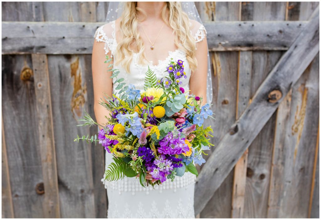 Bridal portrait of her colorful bouquet in front of a barn door at Lewis Farm | Asheville Wedding Photographer