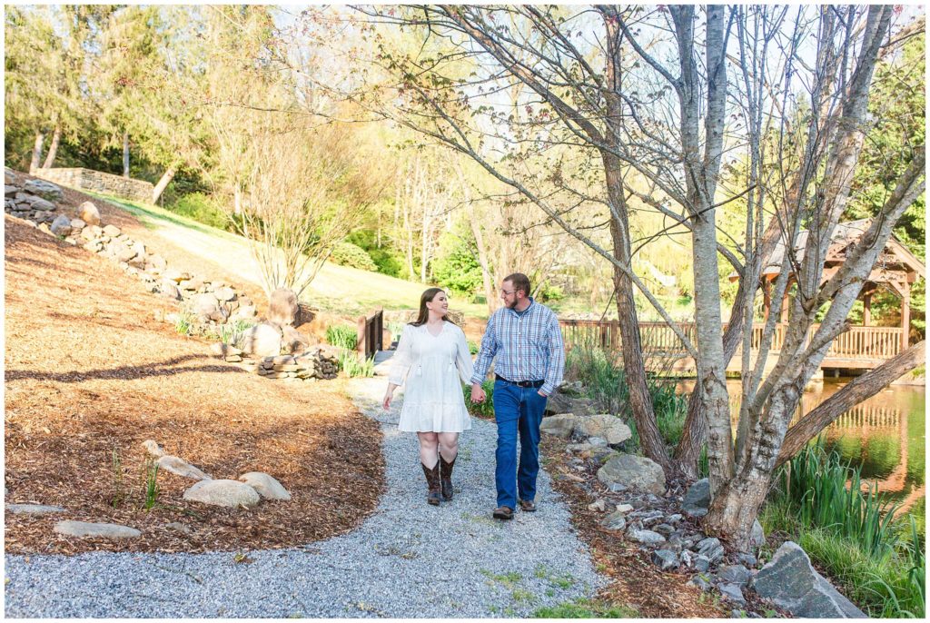 Hannah and Lane hold hands walking through the gardens at Honeysuckle Hill | Asheville Engagement Photographer