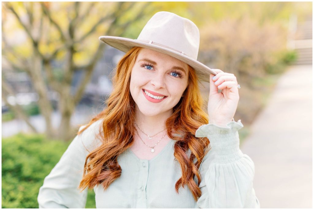 High school senior girl with red hair holding a tan hat on her head