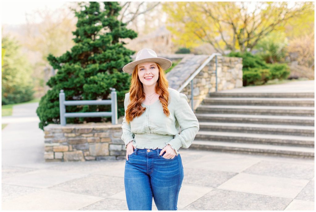 High school senior photos of a girl wearing jeans and a green shirt with a tan hat, with her hands in her pockets.