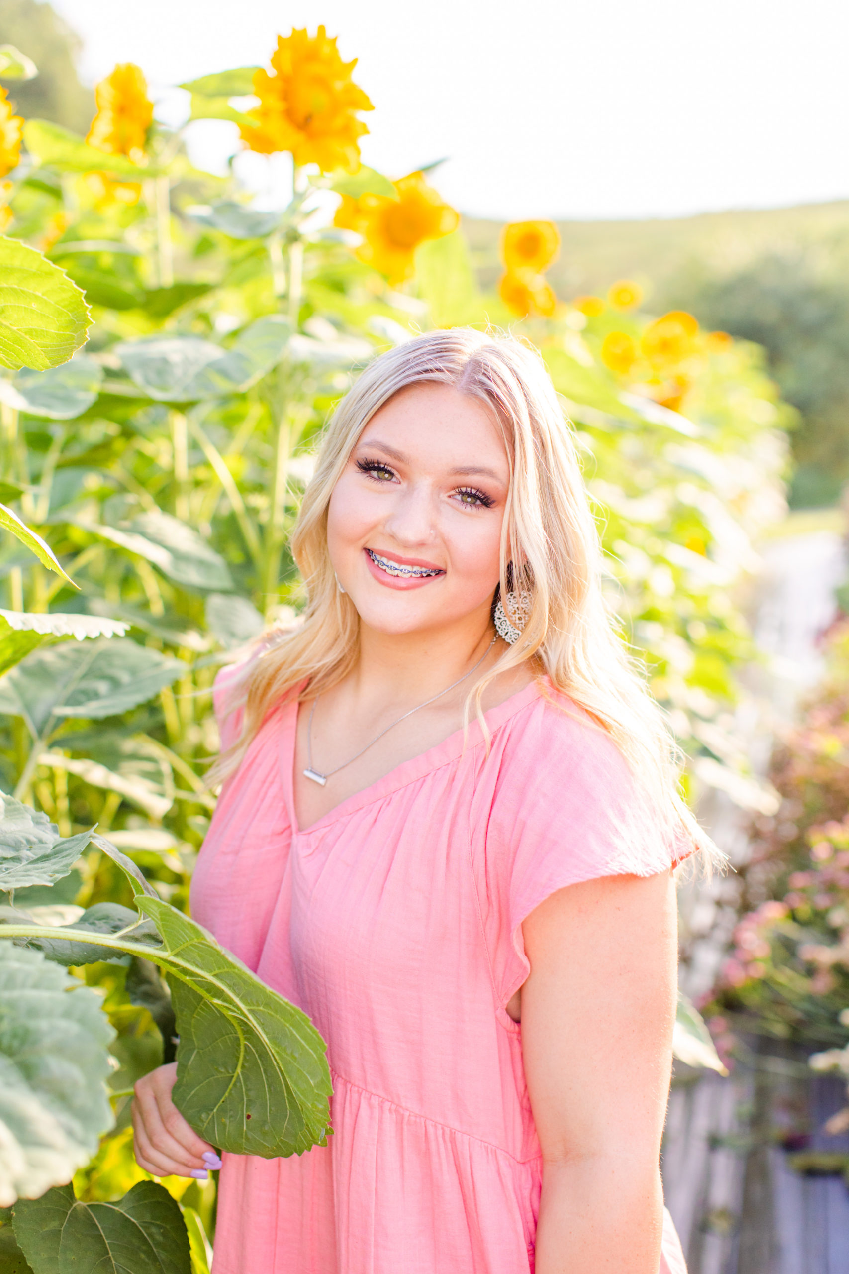 high school senior standing in front of sunflowers in pink dress for senior session at flower farm