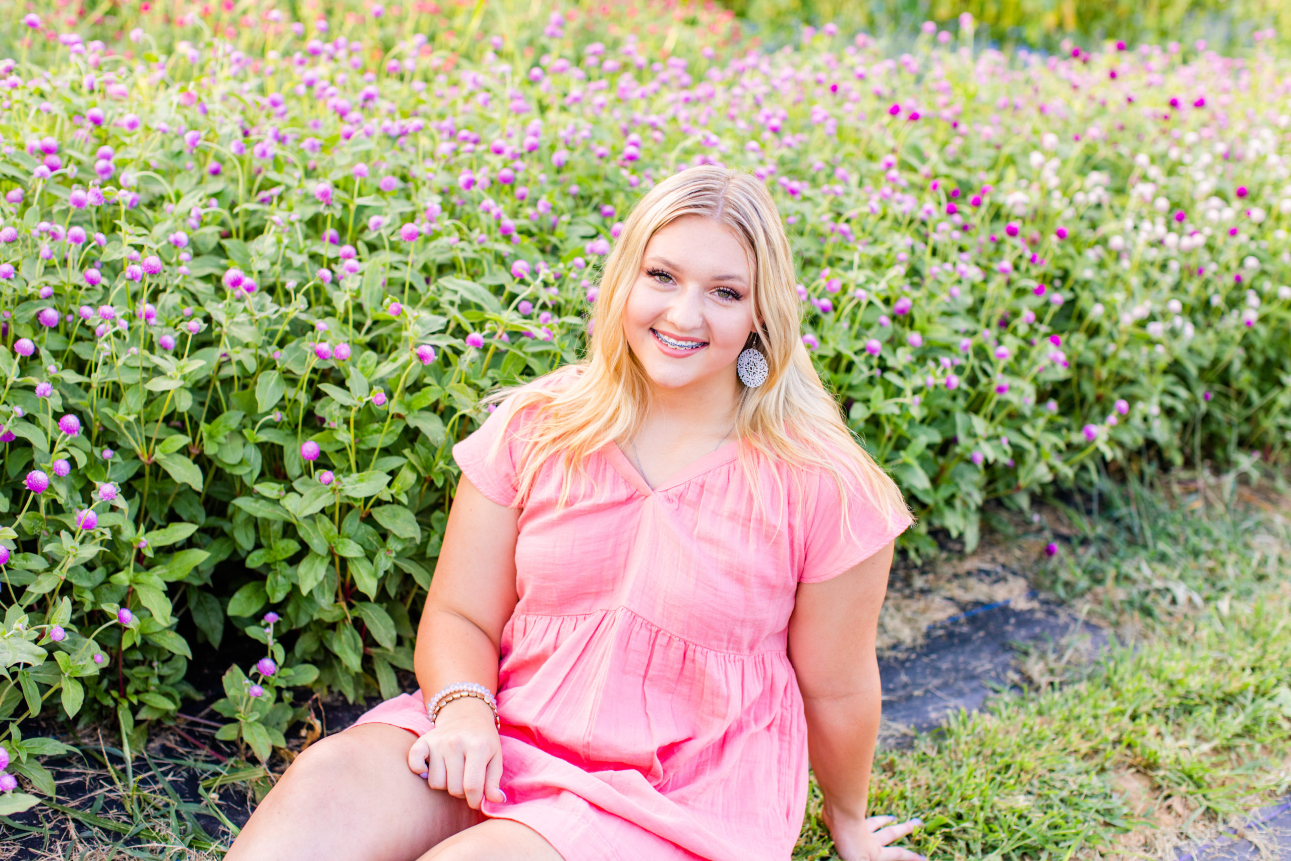 high school senior girl wearing pink dress sitting in a field at a flower farm