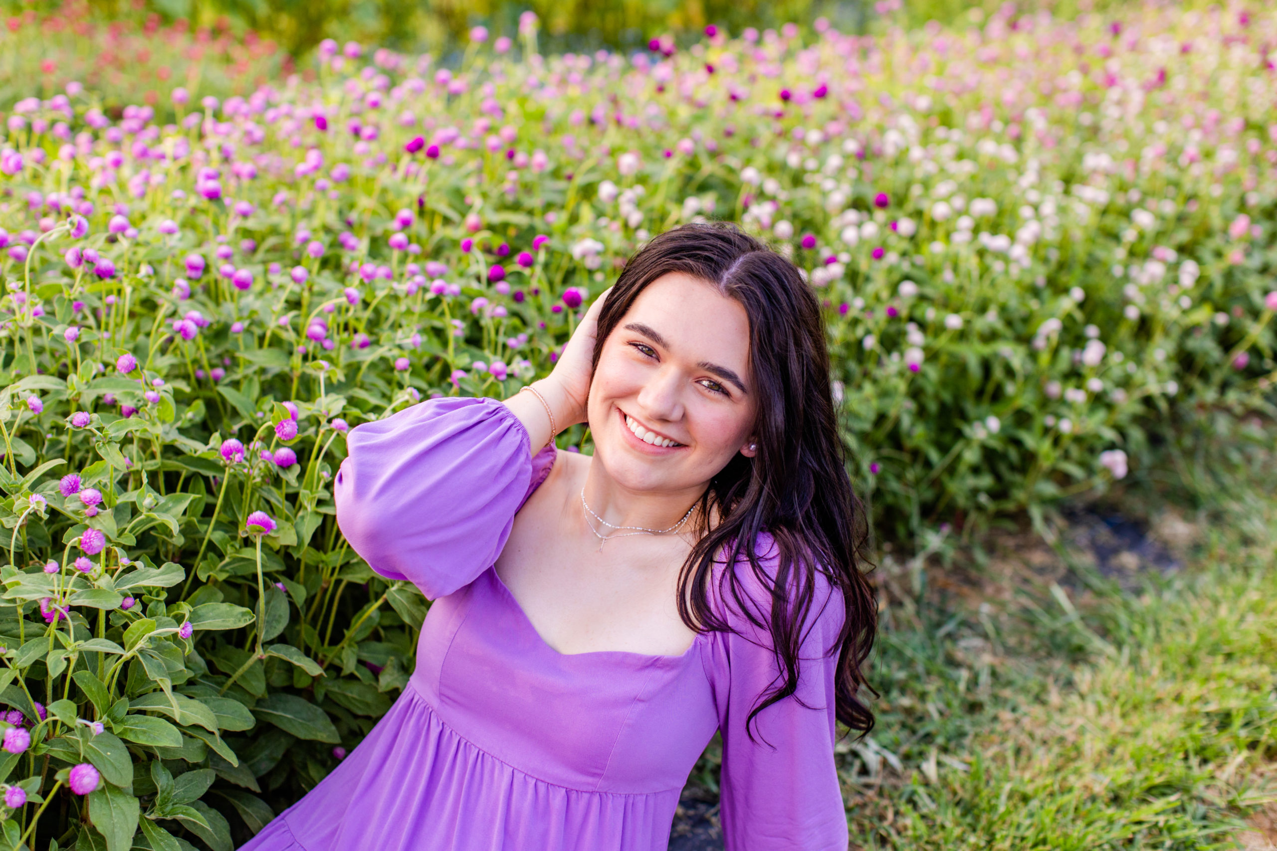 high school senior girl wearing purple dress sitting in a field at a flower farm