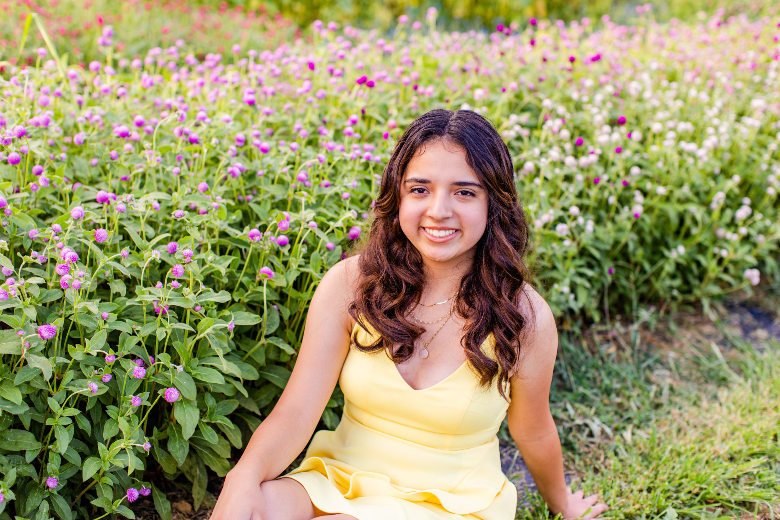 high school senior girl wearing yellow dress sitting in a field at a flower farm