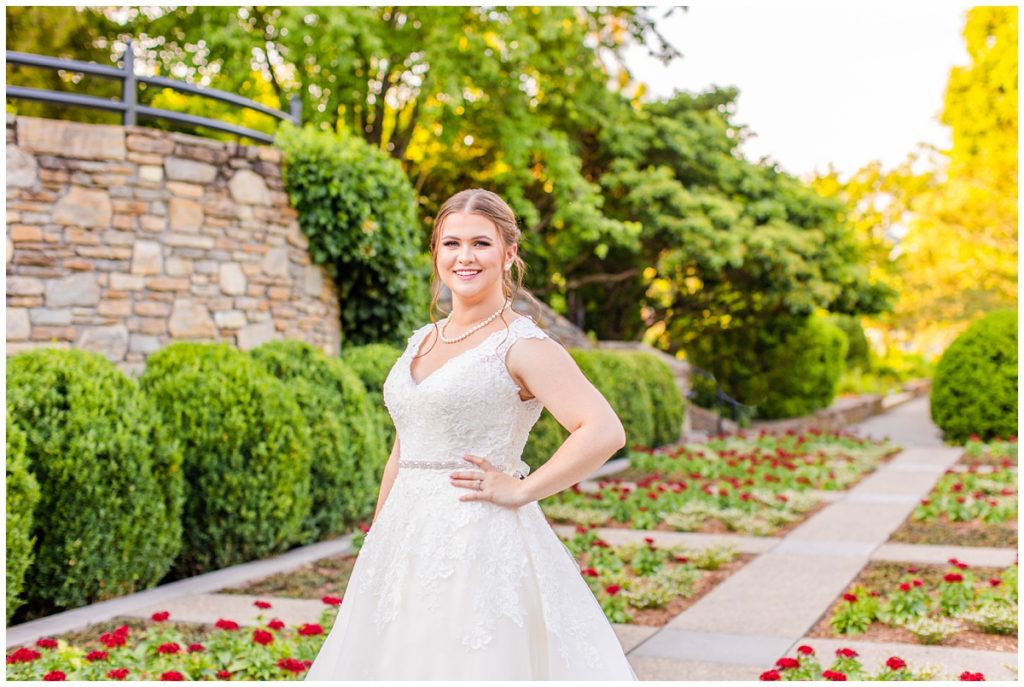 bride poses at the NC Arboretum for her bridal portraits in front of red roses