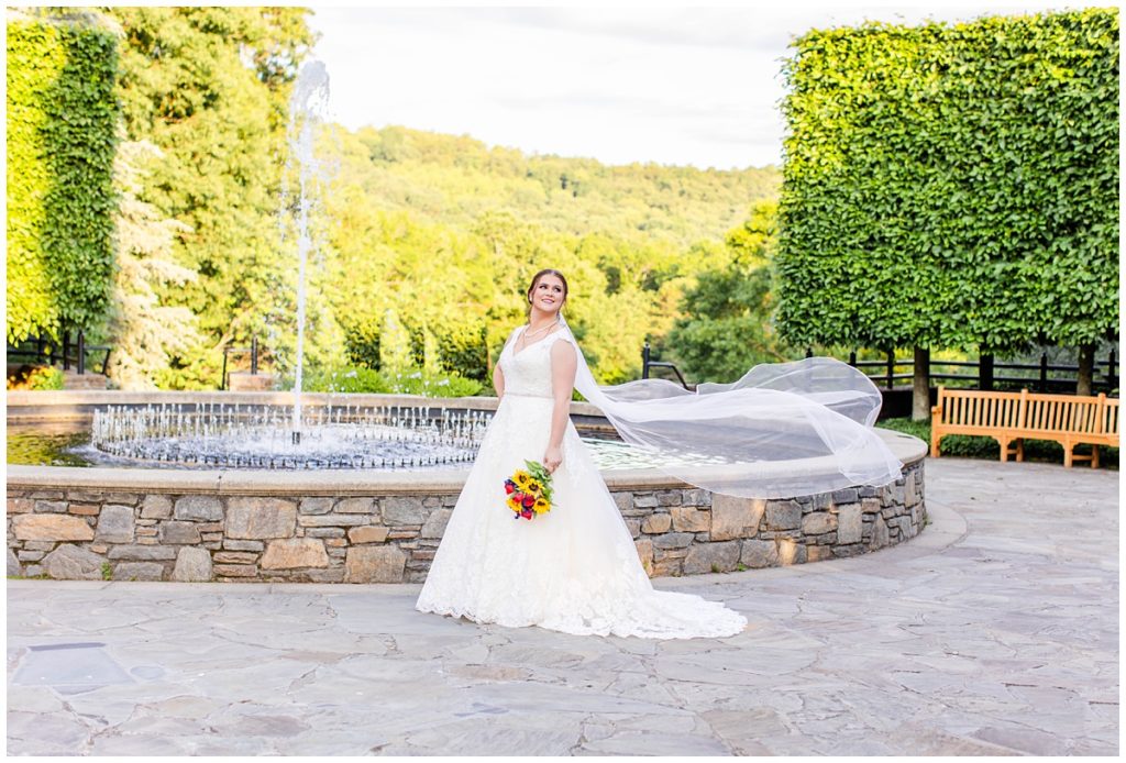 bride holds bouquet in front of fountain at the NC Arboretum
