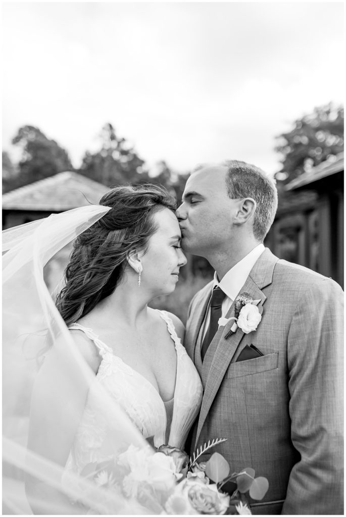 black and white photo of a bride and groom with groom kissing bride's head