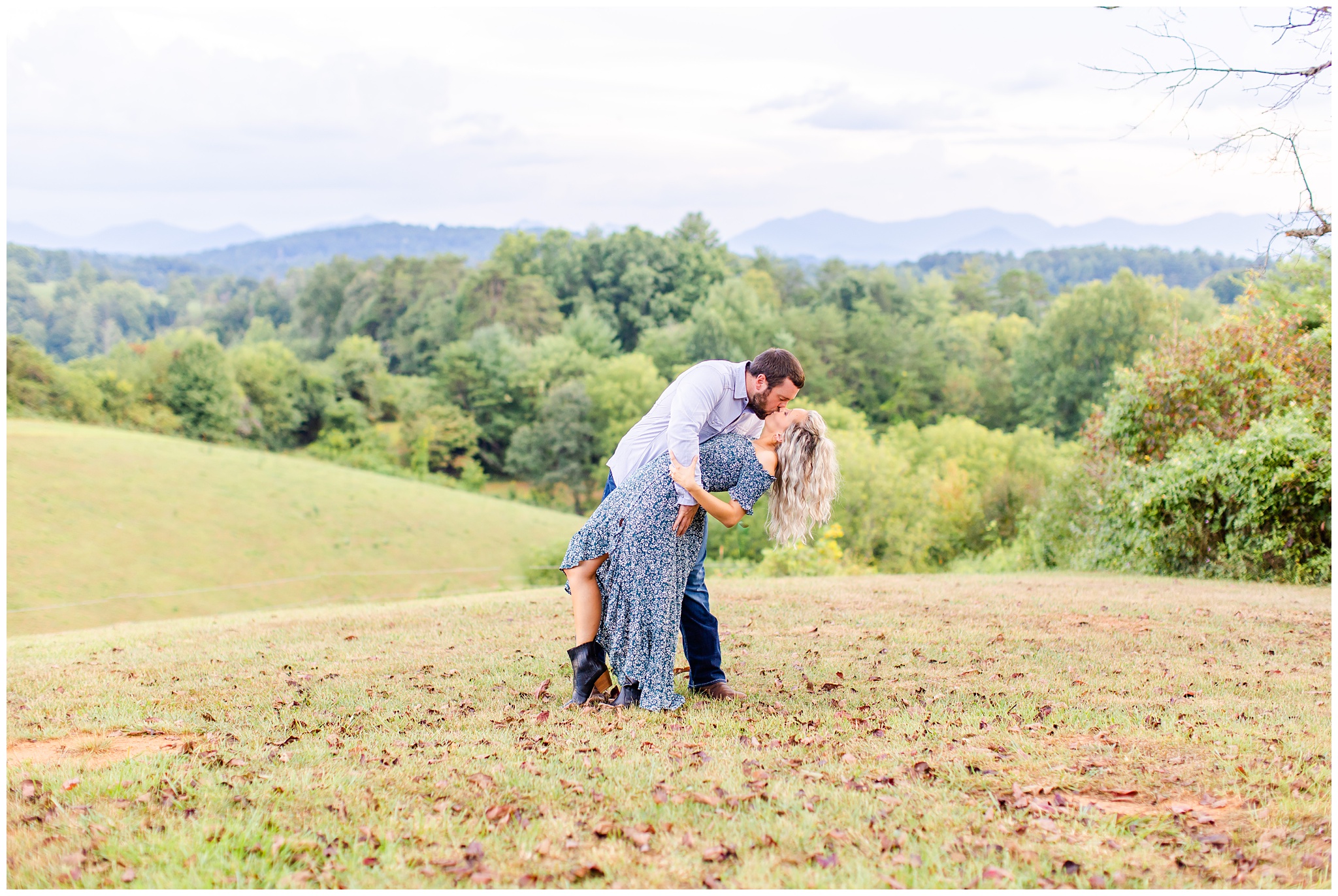 couple shares a dip kiss on a hillside with mountains behind them for photo shoot