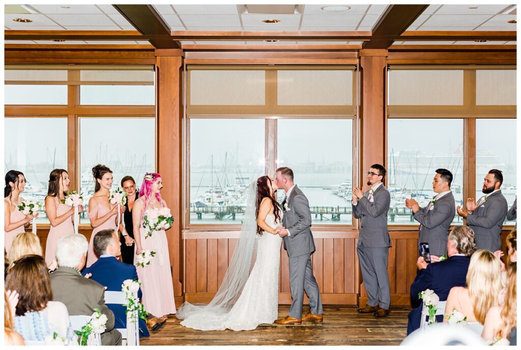 bride and groom first kiss with sailboats behind them at Charleston Harbor and Resort